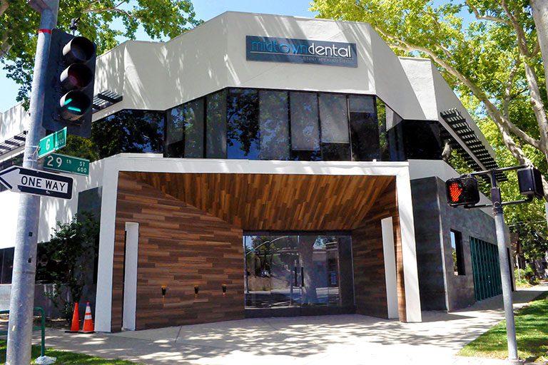 The Midtown Dental office building is painted off-white with a wood-paneled awning surrounding the front door on three sides.